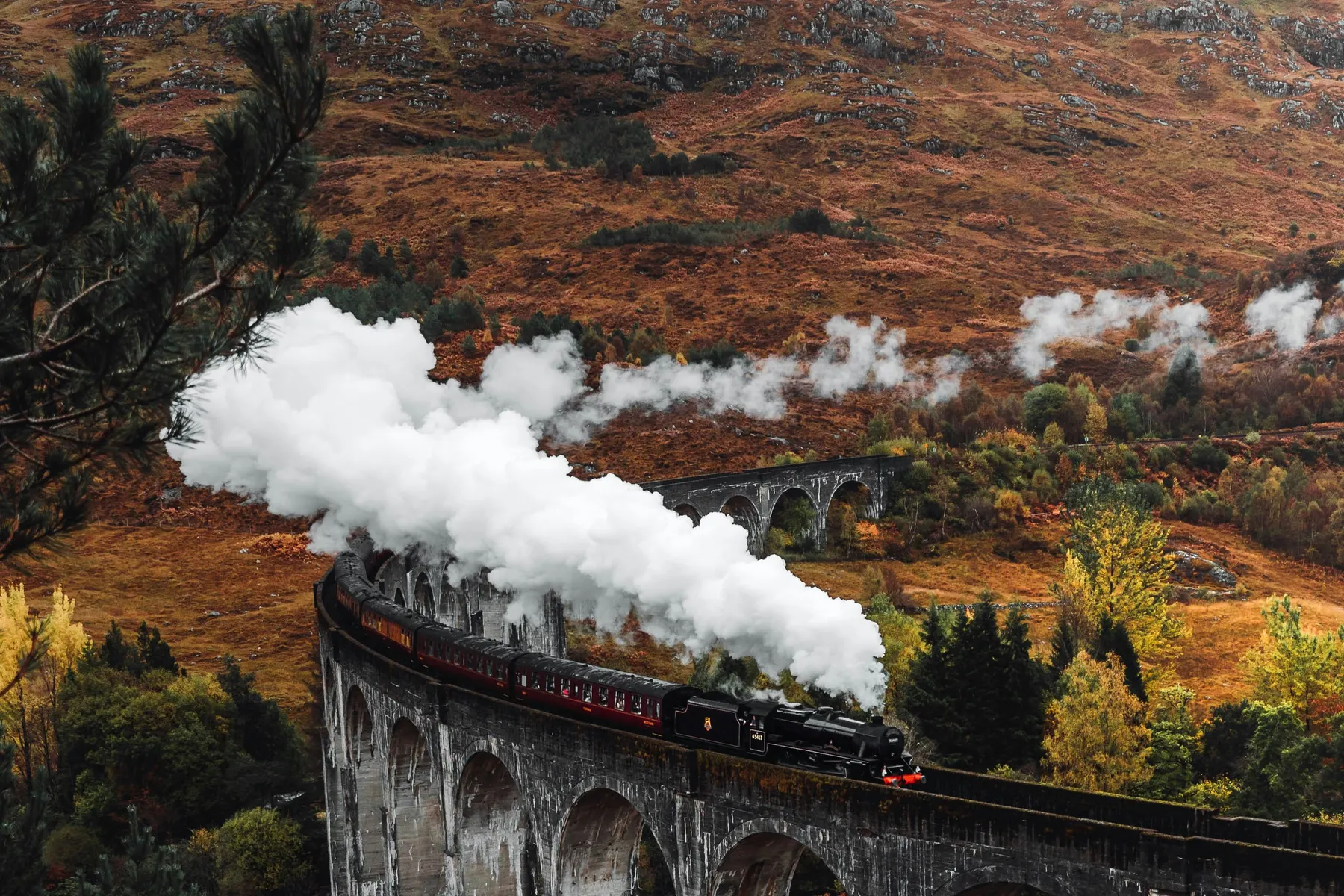 A steam train crossing the Glenfinnan Viaduct through autumn hillsides